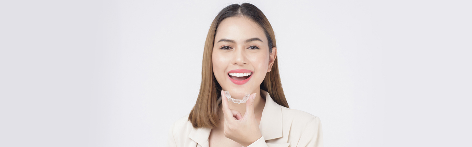 A smiling lady holding Invisalign clear aligners in hand